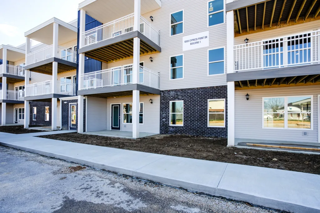 Cypress Point in Washington, Indiana: a multi-storey apartment building with gray and blue siding, dark brick at ground level, white balcony railings and a concrete walkway along the front.