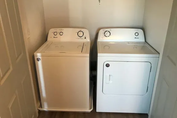 The laundry space in a Parkside Manor apartment: a top loading washing machine and a dryer standing side by side in an alcove.