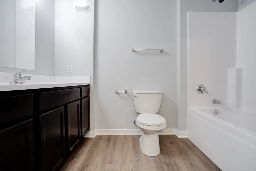 A Cypress Point bathroom with a wood vanity, white counter, toilet and bathtub with shower surround.