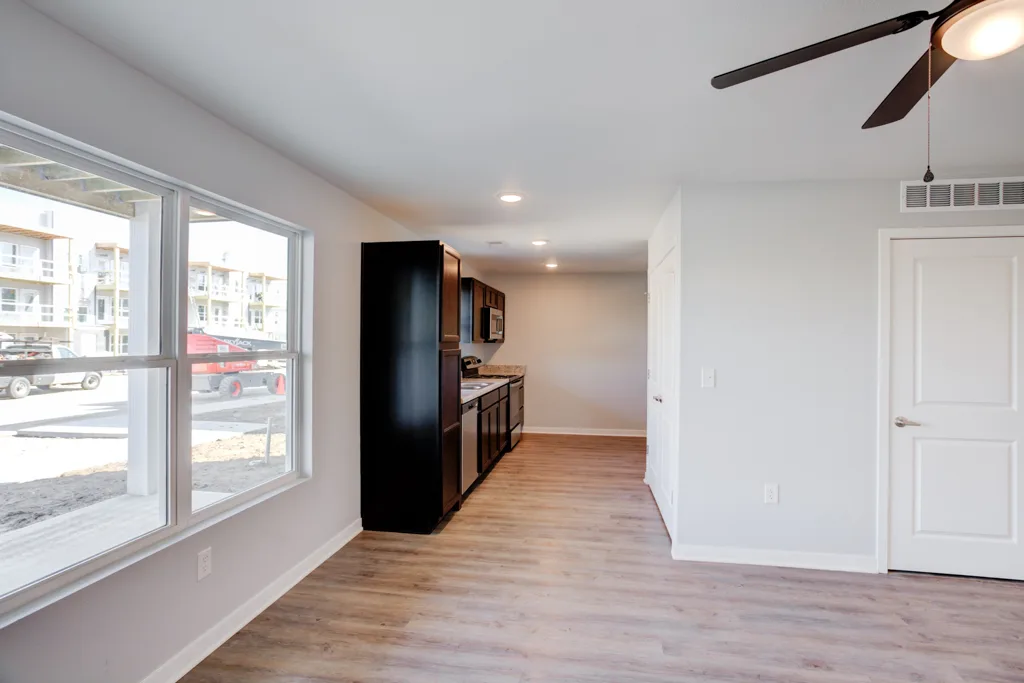 An open Cypress Point apartment interior with a kitchen island, dark cabinets and a living area beyond.