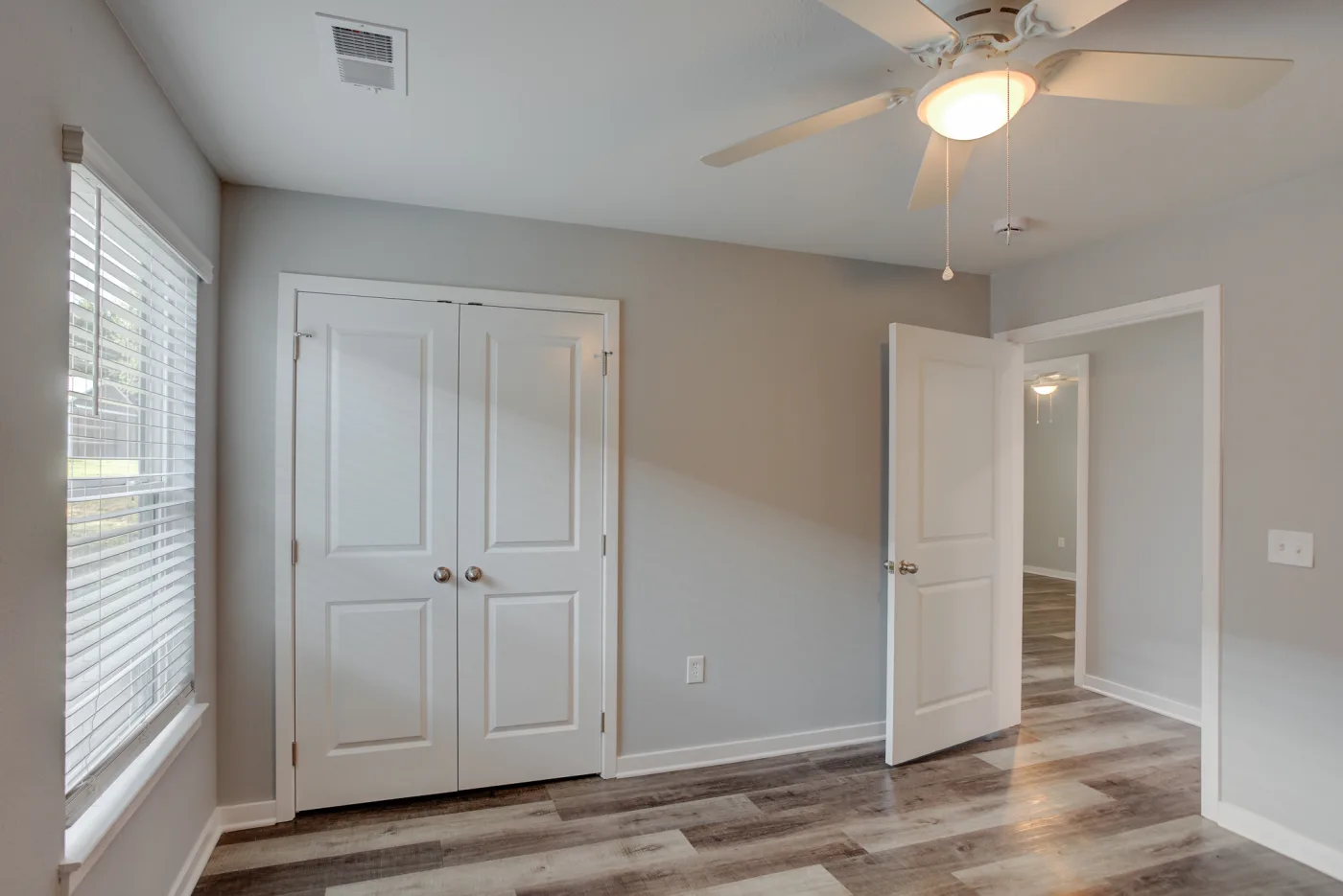 An unfurnished Orchard Estates bedroom with a window, ceiling fan, double-door closet and wood-look flooring.