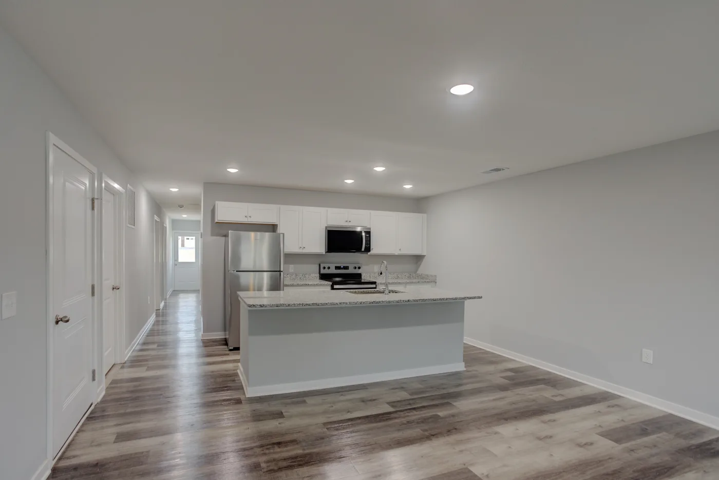 An Orchard Estates kitchen with white cabinets, stainless steel appliances, an island and wood-look flooring.